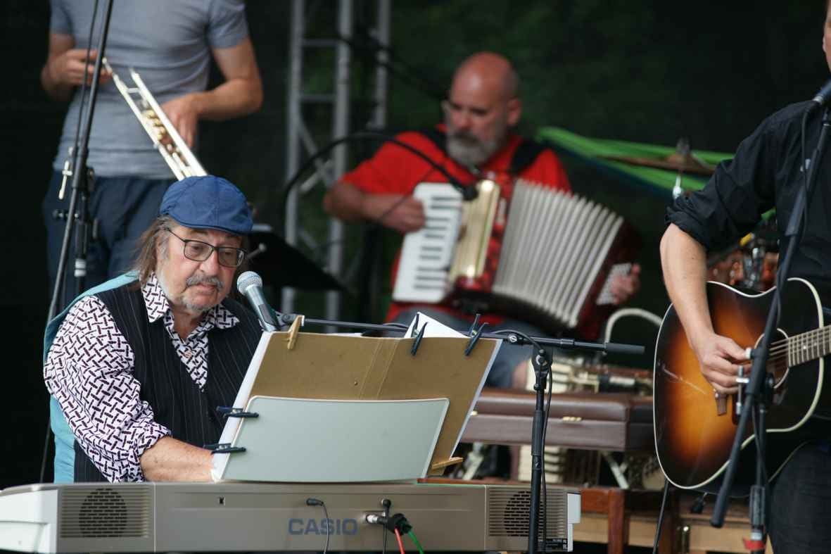 Das Liedertour-Festival, 31.07.2021: Programm „Heimatkunde“ mit Ralph Schüller und Band und Manfred Maurenbrecher (vermutlich am Keyboard, mit Mütze), Akkordeon, Trompete, Open-Air-Bühne