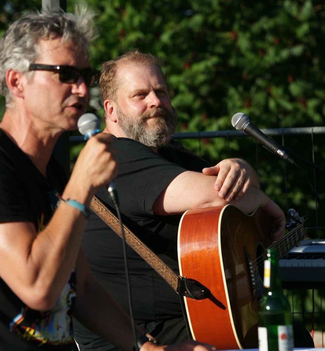 Das Liedertour-Festival, 30.07.2021: musikalische Lesung Mark Daniel und Gunter Schwarz (Akustikgitarre), zwei Männer am Mikrofon, Laub im Hintergrund