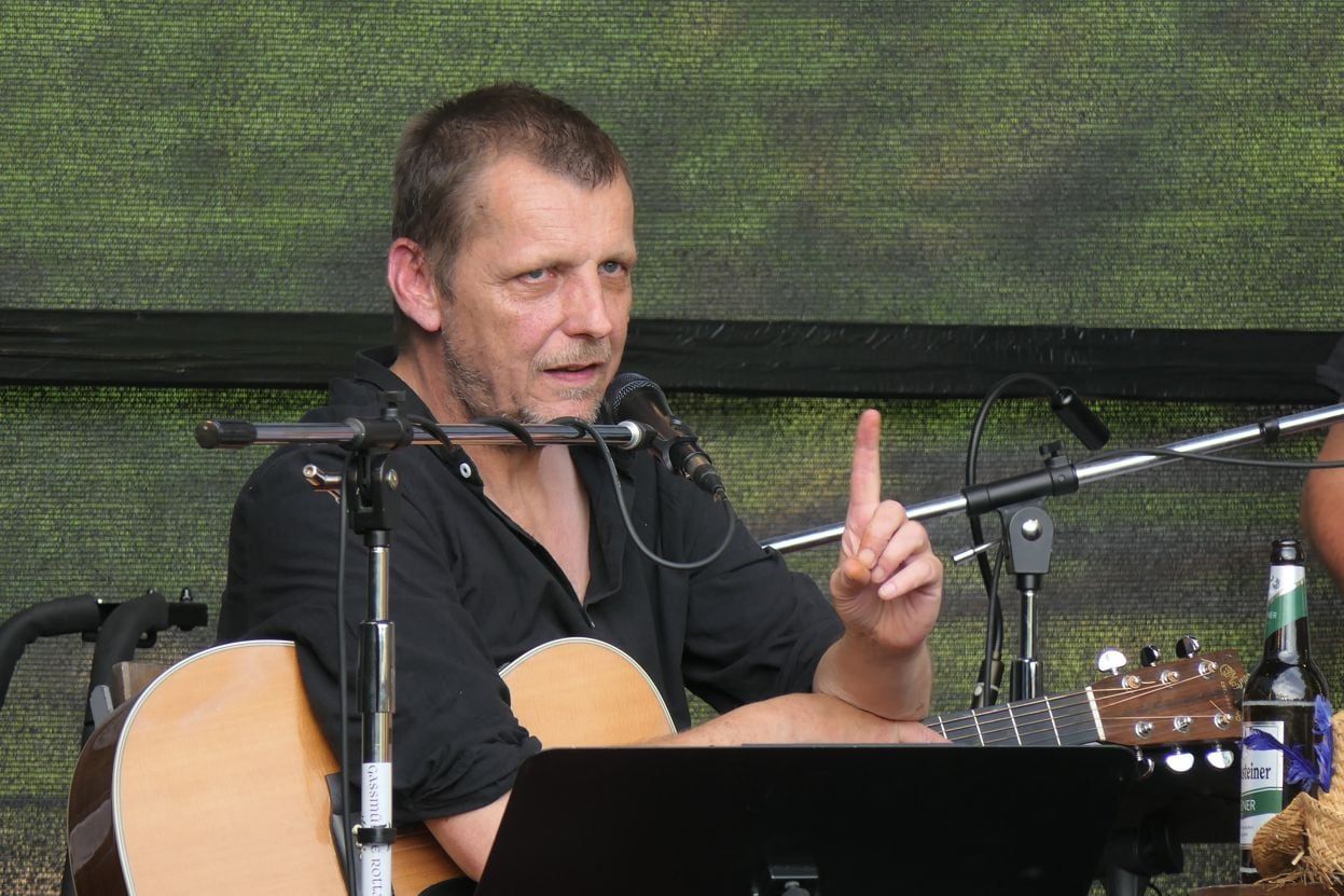 Liedertour-Festival, Gassmühle Rotta, 26.07.2025: Sänger mit Akustikgitarre im schwarzen Hemd am Mikrofon (Band Schüller, vermutlich Ralph Schüller), erhobener Zeigefinger