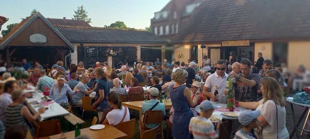 Hofkonzert der Liedertour in Lindow: das Publikum an langen Tischen, hinten die Bühne mit dem Liedertour-Schild